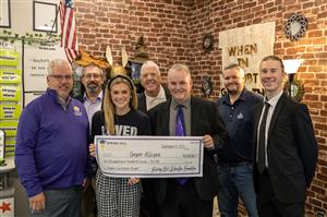 Cooper Allison holding a novelty check & SHEF Board smiling for the Teacher Excellence Grant presentation at WSMS